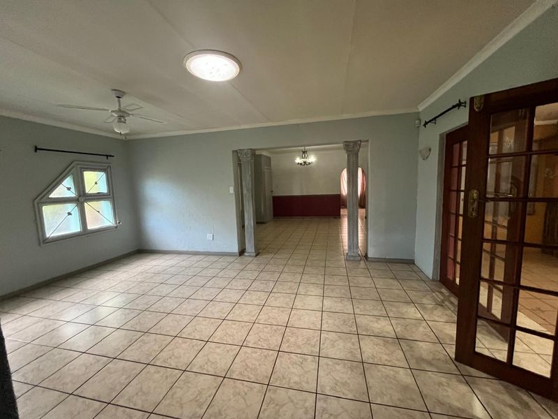 Spacious living area featuring tiled flooring, decorative columns, and a ceiling fan, offering an open-plan layout with access to adjacent rooms through french doors.