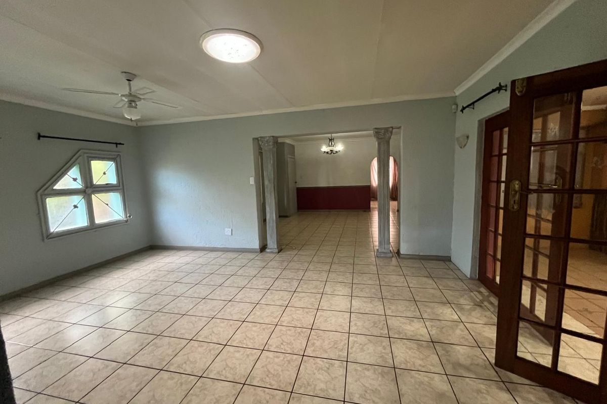 Spacious living area featuring tiled flooring, decorative columns, and a ceiling fan, offering an open-plan layout with access to adjacent rooms through french doors.