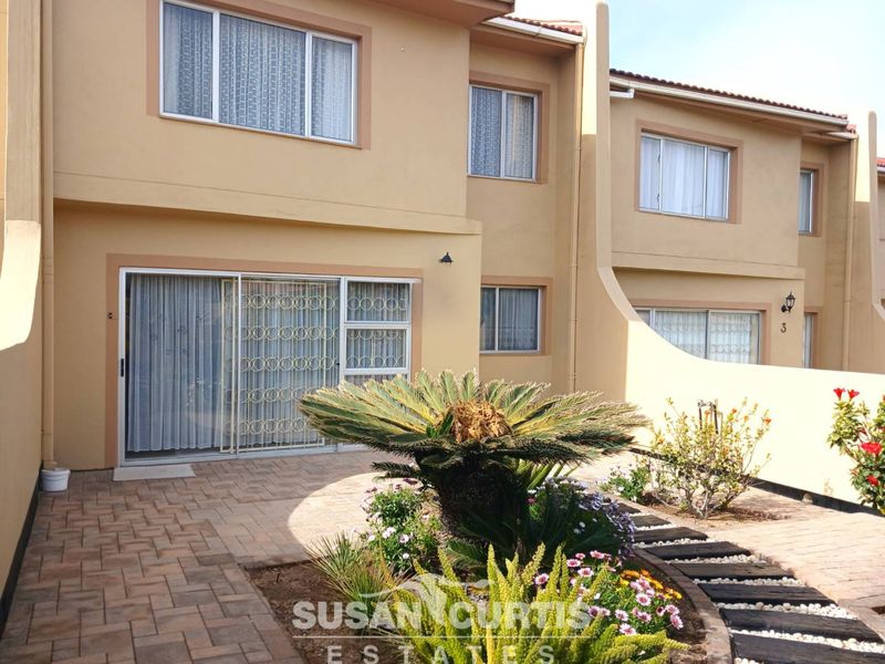 Rear view of the townhouse featuring a paved patio area, sliding glass doors with security gates, and established garden landscaping.