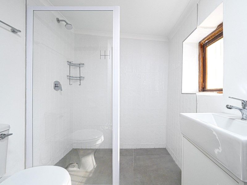 A clean, functional bathroom featuring a glass-enclosed shower, white vanity basin, and neutral tiled finishes throughout.