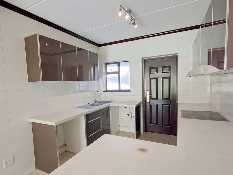 A clean, modern kitchen featuring high-gloss cabinetry, white tiled walls, a built-in electric hob, and a stainless steel sink.