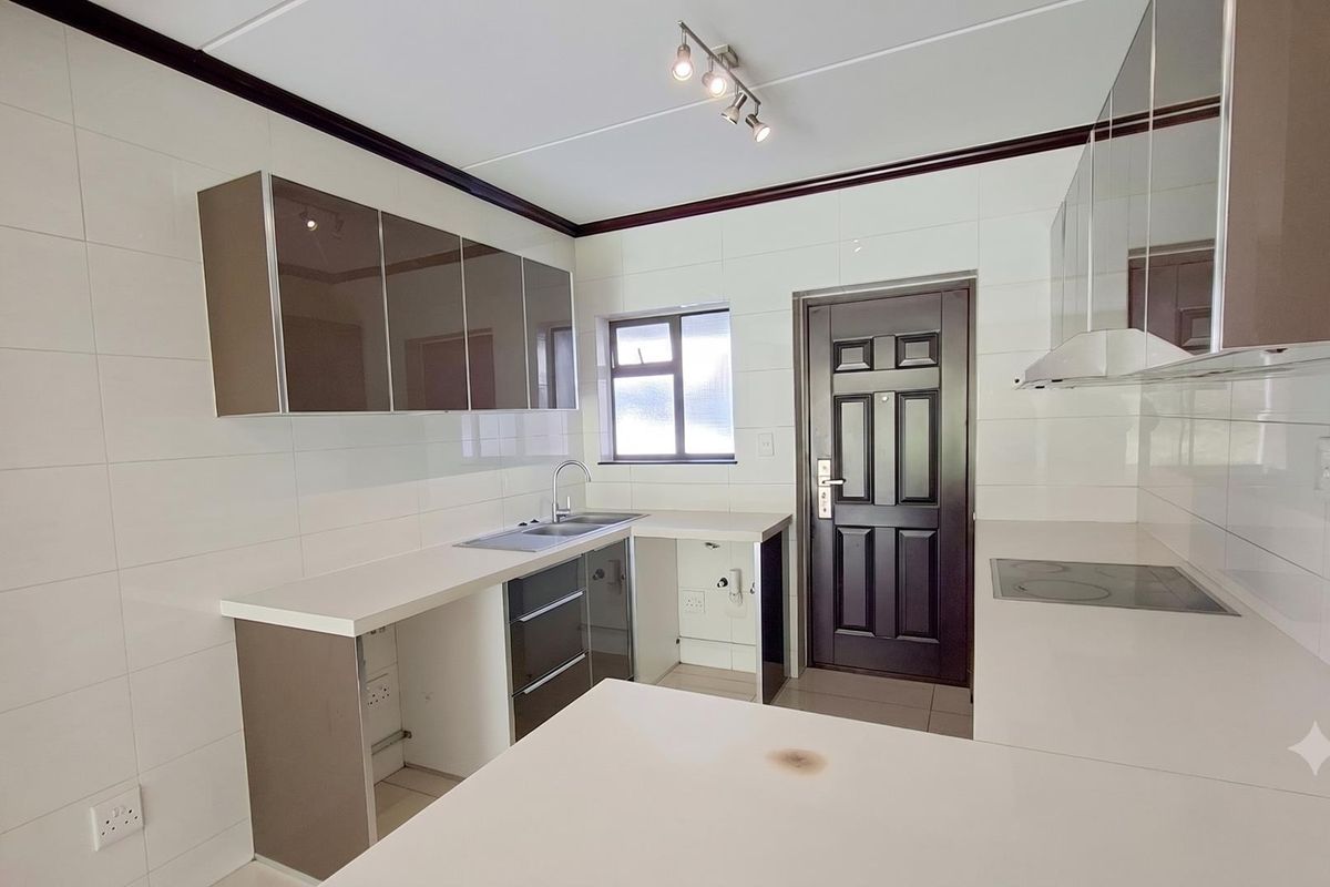 A clean, modern kitchen featuring high-gloss cabinetry, white tiled walls, a built-in electric hob, and a stainless steel sink.