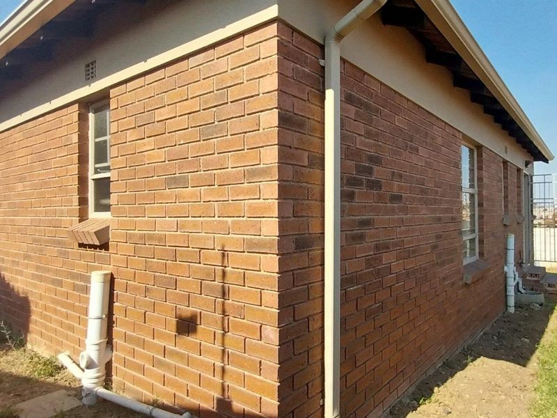 Rear exterior view of the house featuring face brick walls, external plumbing, and a precast concrete boundary wall.