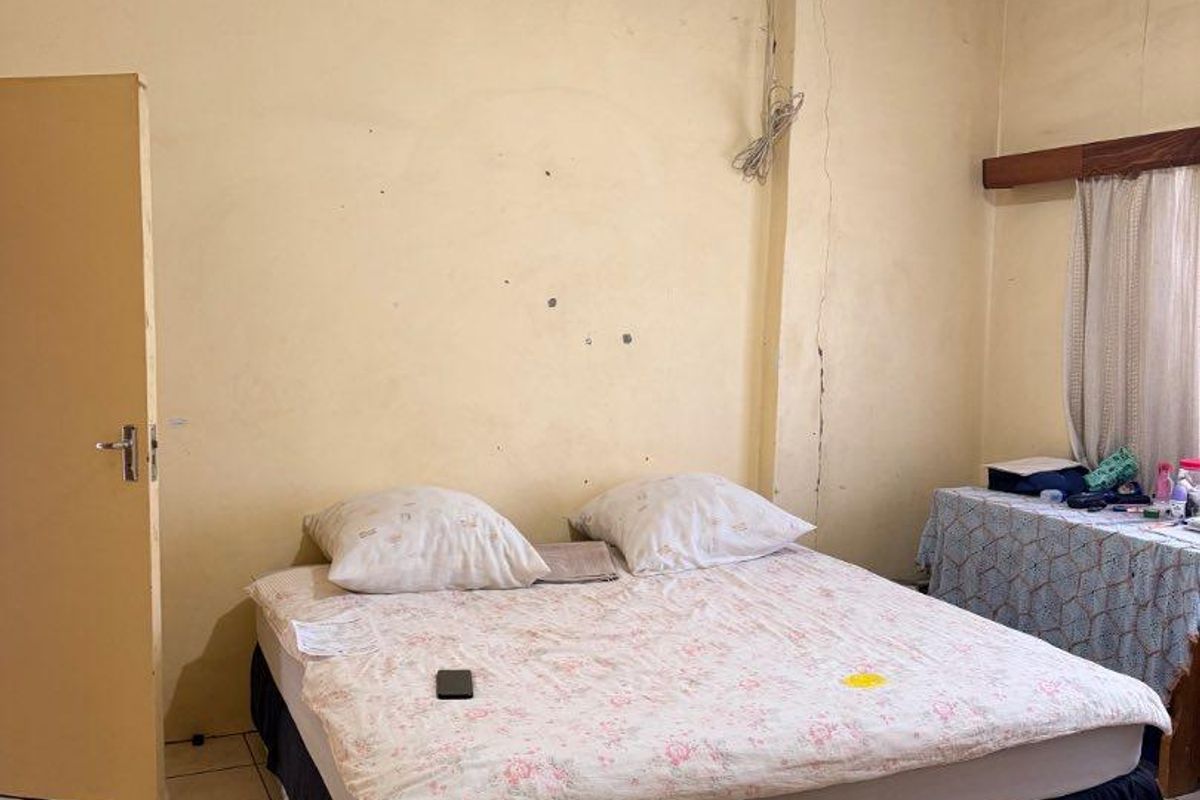 A bedroom featuring tiled flooring and a standard door, currently showing signs of wear including wall cracks and surface imperfections.