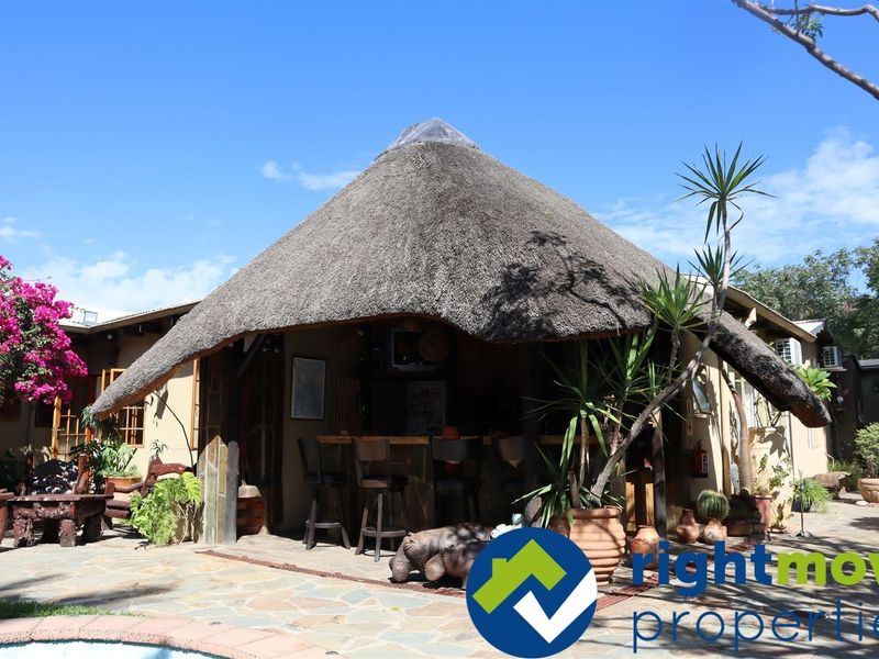 A charming outdoor entertainment area featuring a traditional thatched roof structure and a built-in bar, set on stone paving overlooking the pool area.