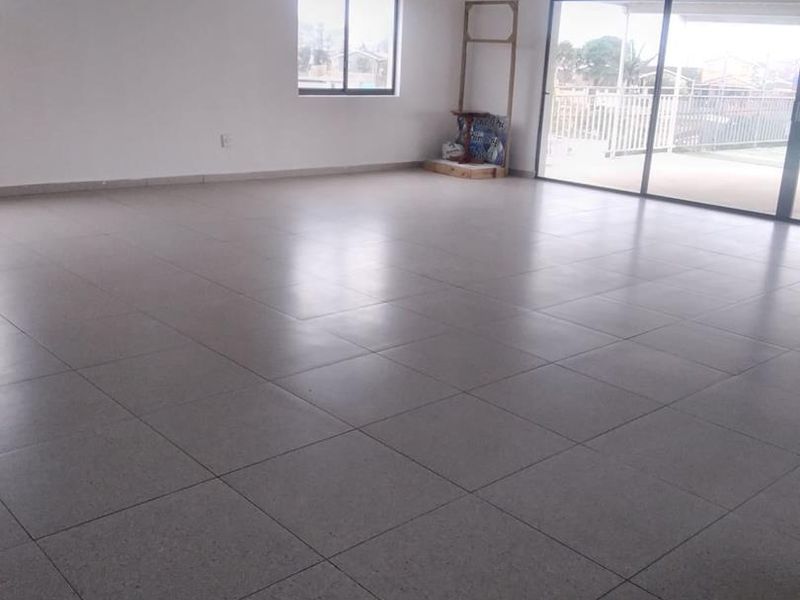 A spacious, empty living area featuring neutral tiled flooring, recessed ceiling lights, and large sliding glass doors providing access to an outdoor patio.