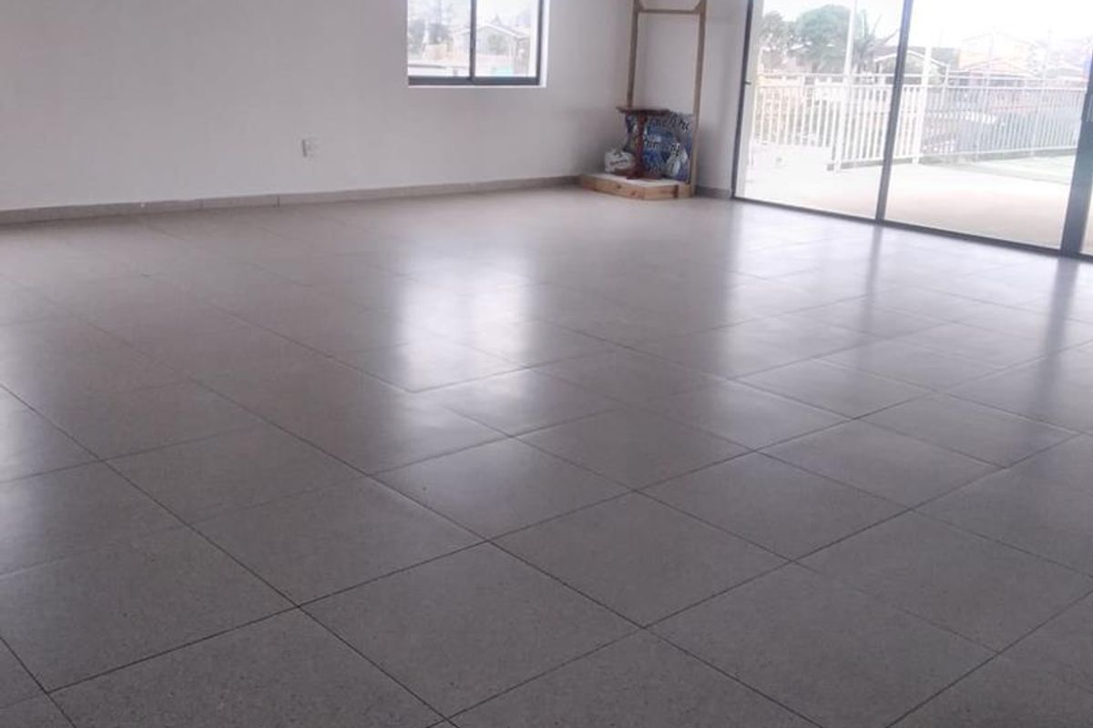 A spacious, empty living area featuring neutral tiled flooring, recessed ceiling lights, and large sliding glass doors providing access to an outdoor patio.