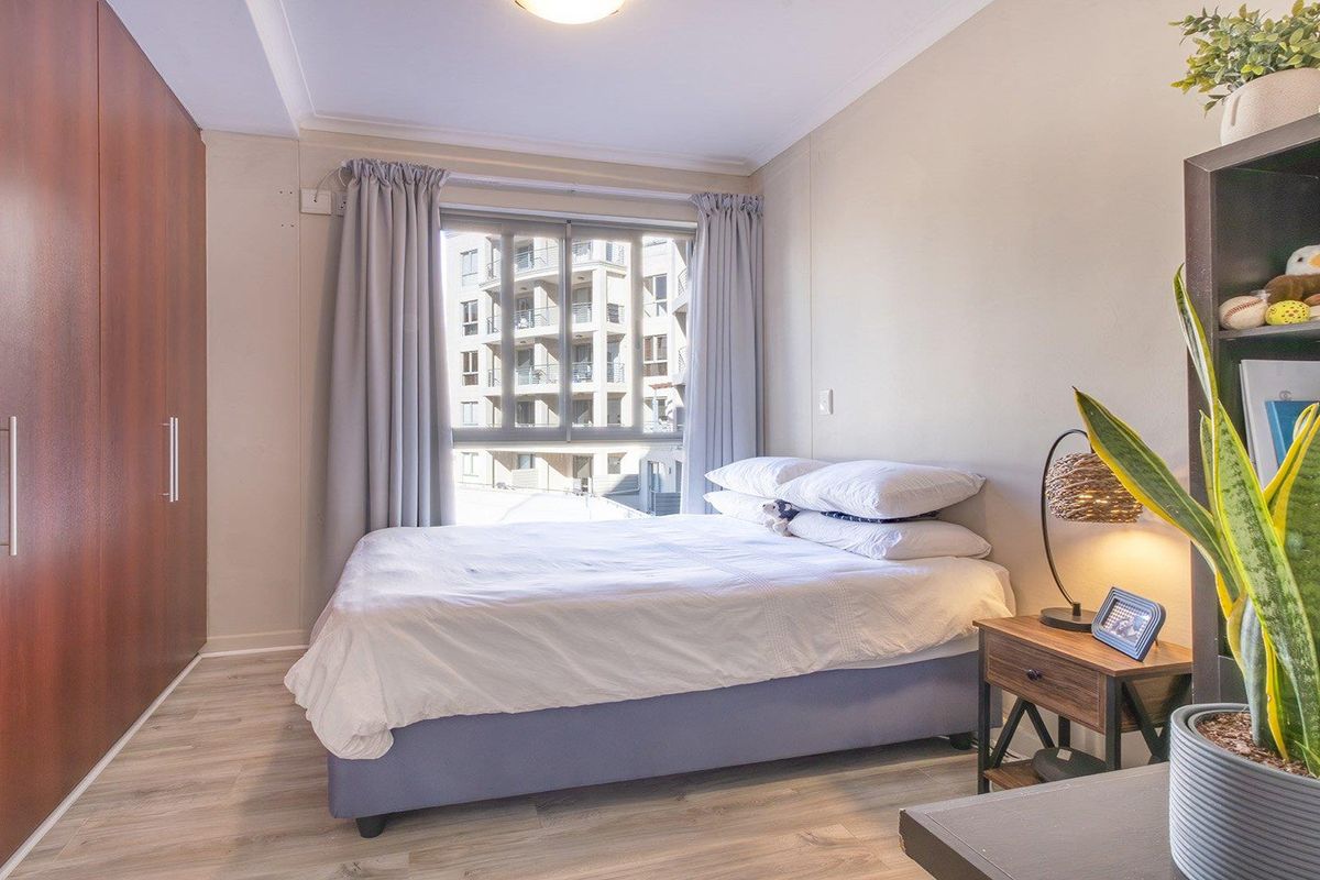 A well-maintained bedroom featuring light laminate flooring, a large built-in wardrobe, and a window providing natural light.