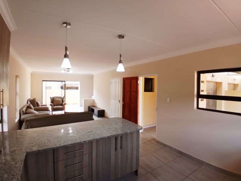 An open-plan living and kitchen area featuring granite countertops, modern cabinetry, tiled flooring, and direct access to an outdoor space through sliding doors.