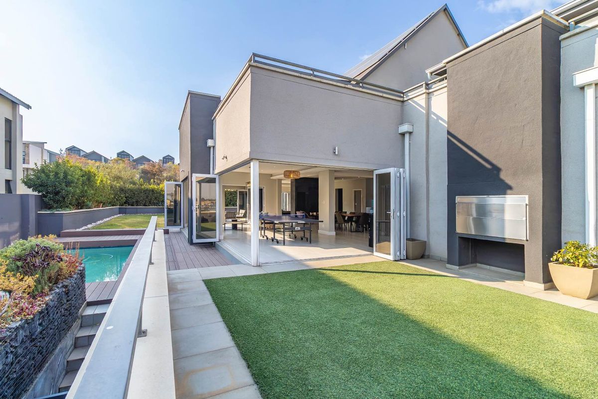 Modern rear exterior featuring a swimming pool, artificial lawn, built-in braai, and seamless indoor-outdoor flow through large bi-fold doors.