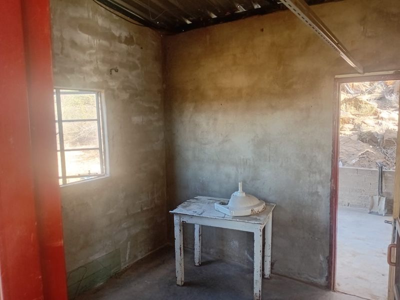 An unfinished utility space featuring exposed cement walls, concrete flooring, and a corrugated metal ceiling, offering a blank canvas for renovation.