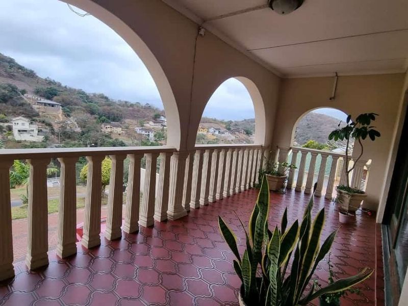 A covered balcony featuring arched architectural details, a classic balustrade, and tiled flooring, offering elevated views of the surrounding landscape.