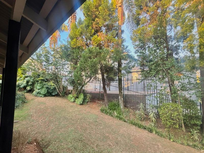 A view of the rear garden featuring a tiled patio area, established trees, and secure metal perimeter fencing.