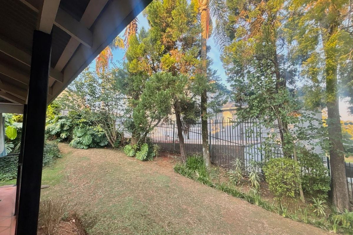 A view of the rear garden featuring a tiled patio area, established trees, and secure metal perimeter fencing.