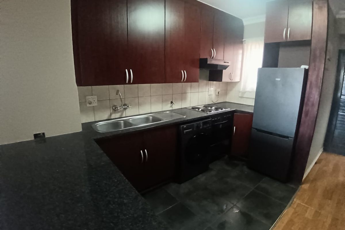 A functional kitchen featuring dark wood cabinetry, granite countertops, a double bowl sink, and built-in cooking appliances with a tiled backsplash.
