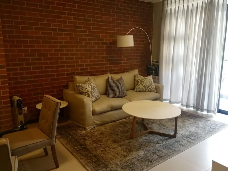 A living room featuring an exposed brick feature wall, tiled flooring, and access to an outdoor area through a sliding glass door.