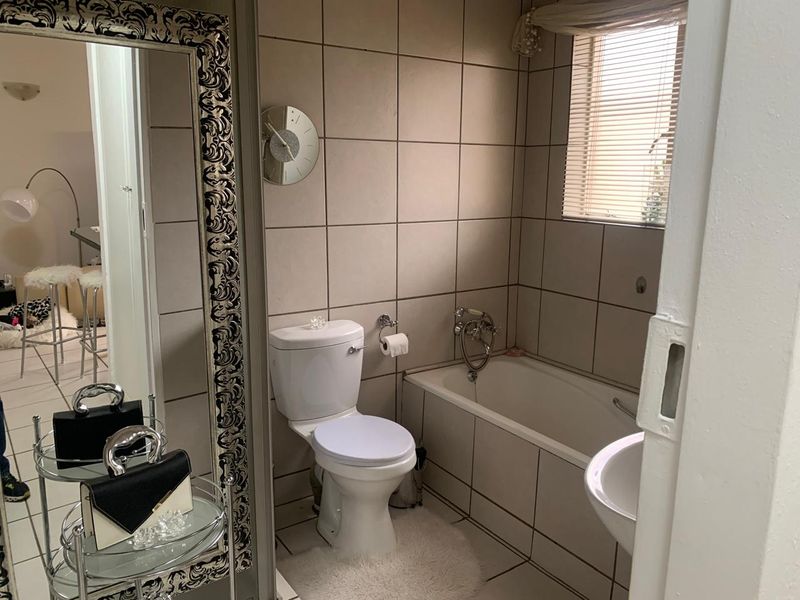 A functional bathroom featuring neutral wall and floor tiles, a built-in bathtub, a pedestal basin, and a standard toilet.