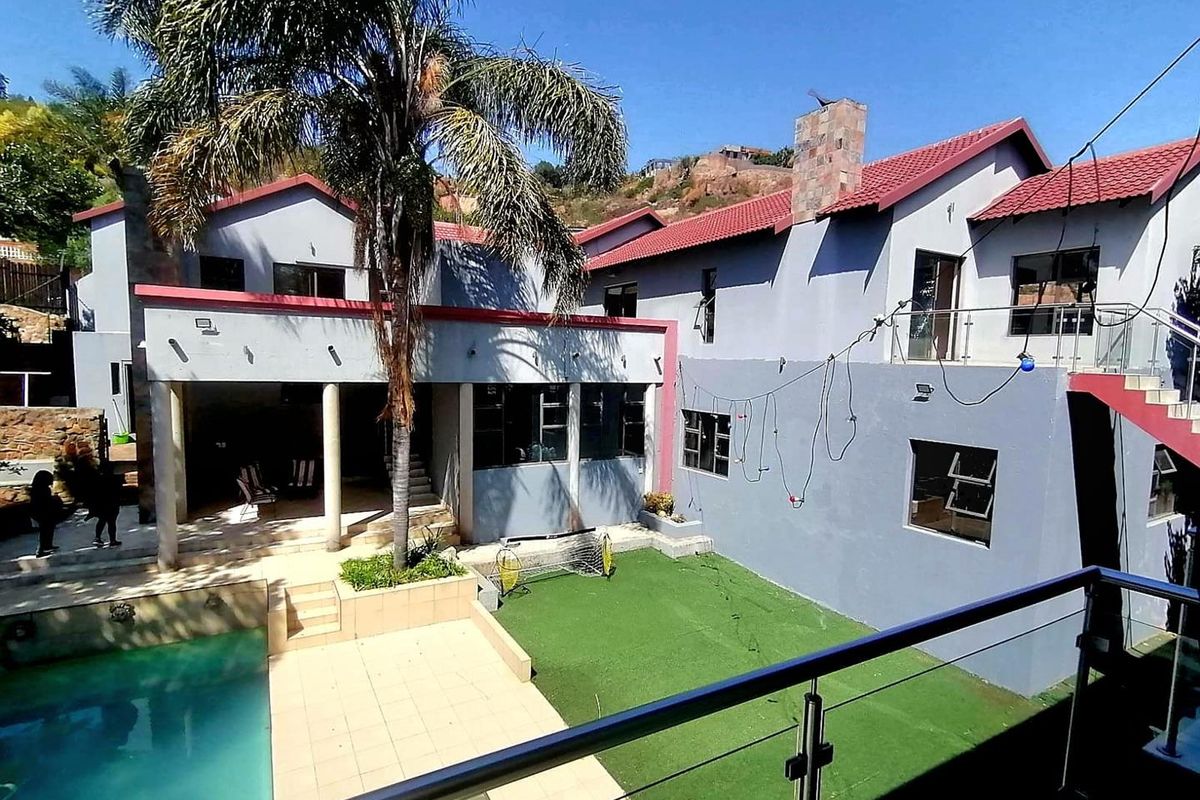 Rear view of the property featuring a swimming pool, tiled patio area, artificial lawn, and an external staircase with glass balustrades.