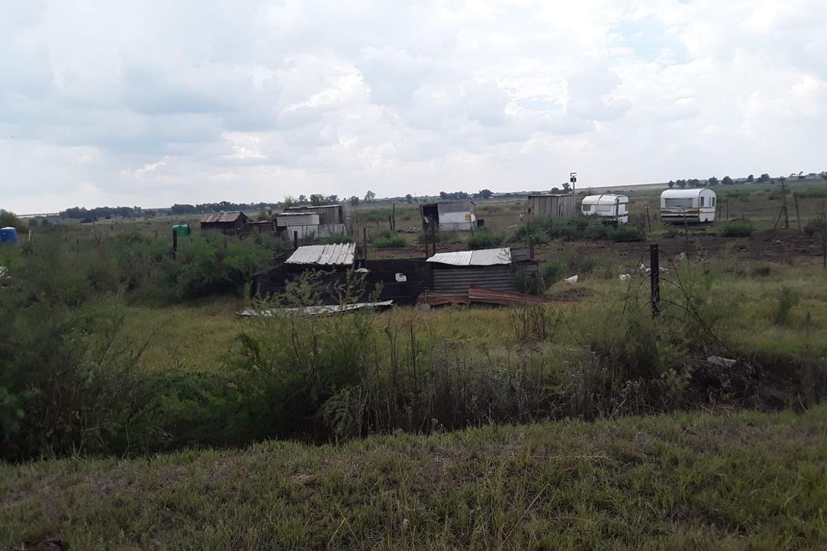 A wide view of the farm property featuring multiple small, dilapidated outbuildings and structures set within an open, undeveloped field.