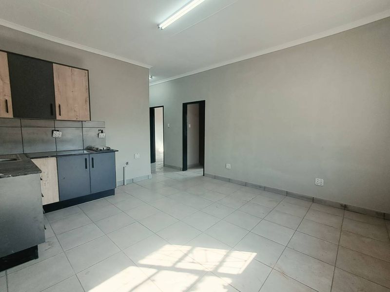 An open-plan living and kitchen area featuring tiled flooring, built-in cabinetry, and neutral wall finishes, offering a blank canvas for interior design.