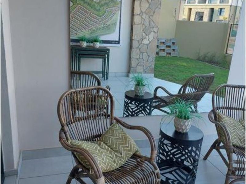 A covered patio area featuring tiled flooring, a stone-clad feature wall, and an exterior light fixture, overlooking a private garden space.