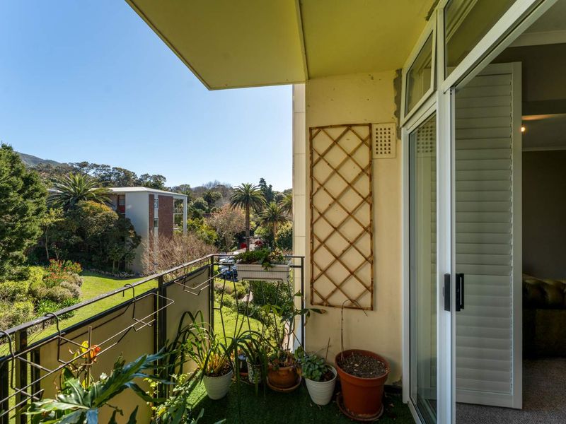 A private balcony featuring a metal balustrade and sliding glass door access, offering pleasant views of the surrounding garden and neighborhood.