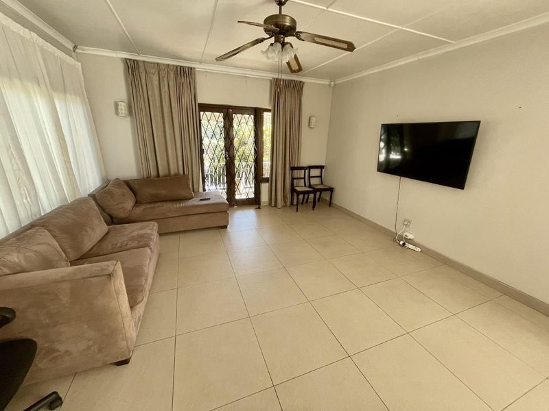 Spacious living room featuring neutral tiled flooring, a ceiling fan, and direct access to the exterior through a secure glass sliding door.