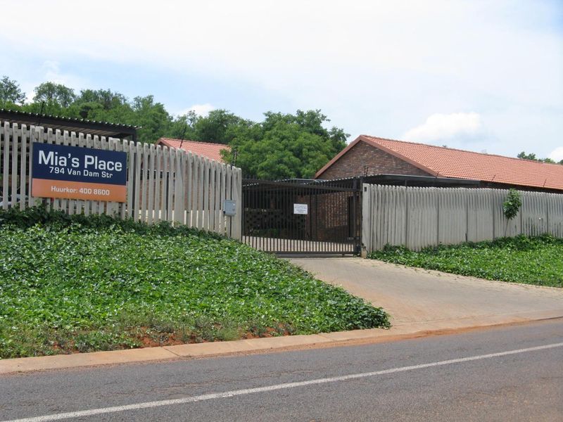 Street view of the apartment complex entrance featuring a paved driveway, secure metal gate, and concrete palisade fencing.