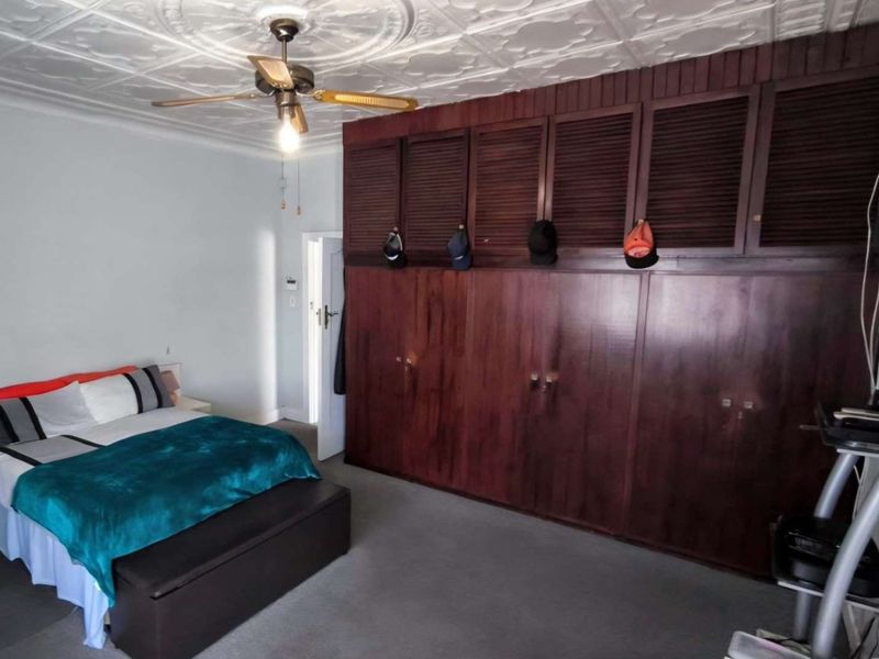 A bedroom featuring a large built-in wooden wardrobe, a decorative pressed metal ceiling with a ceiling fan, and neutral wall finishes.