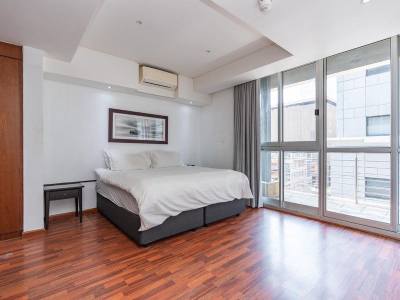 Modern bedroom featuring hardwood flooring, built-in cabinetry, split-system air conditioning, and large sliding glass doors providing access to a private balcony.