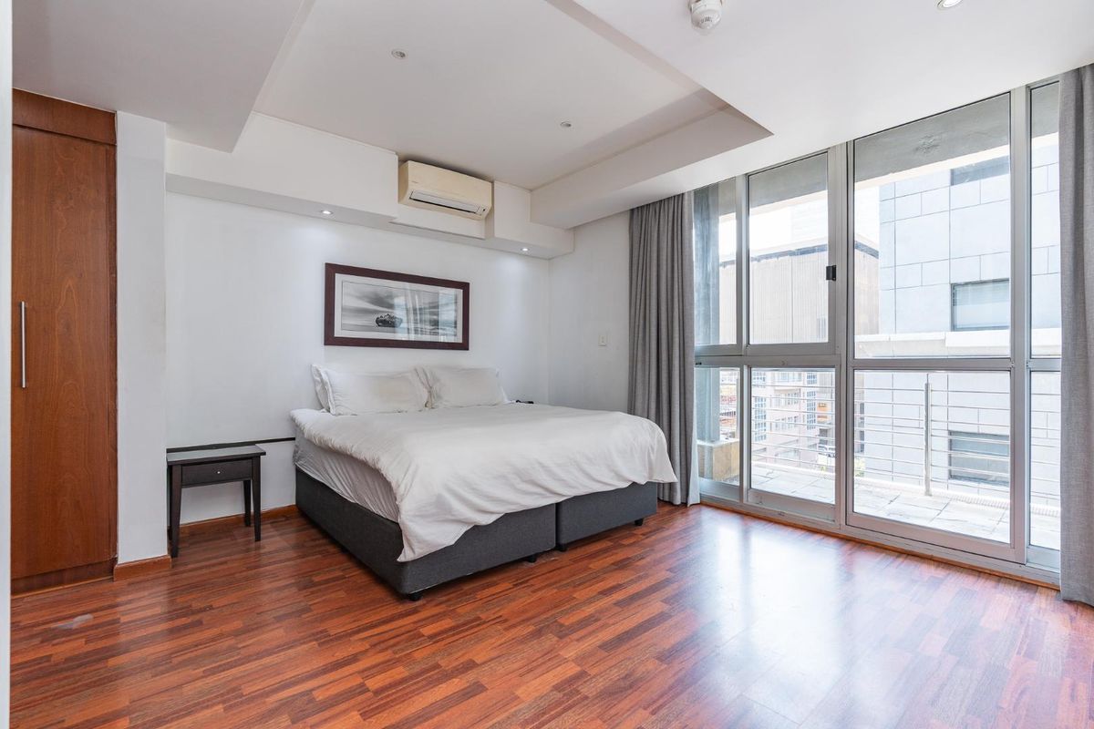 Modern bedroom featuring hardwood flooring, built-in cabinetry, split-system air conditioning, and large sliding glass doors providing access to a private balcony.