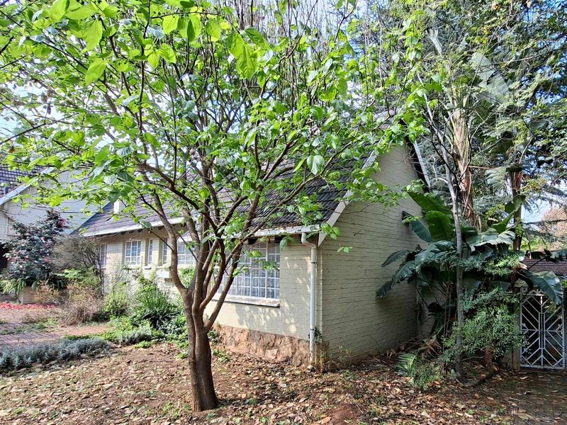Front view of a cottage featuring a brick facade, stone cladding base, and tiled roof, surrounded by mature trees and garden landscaping.
