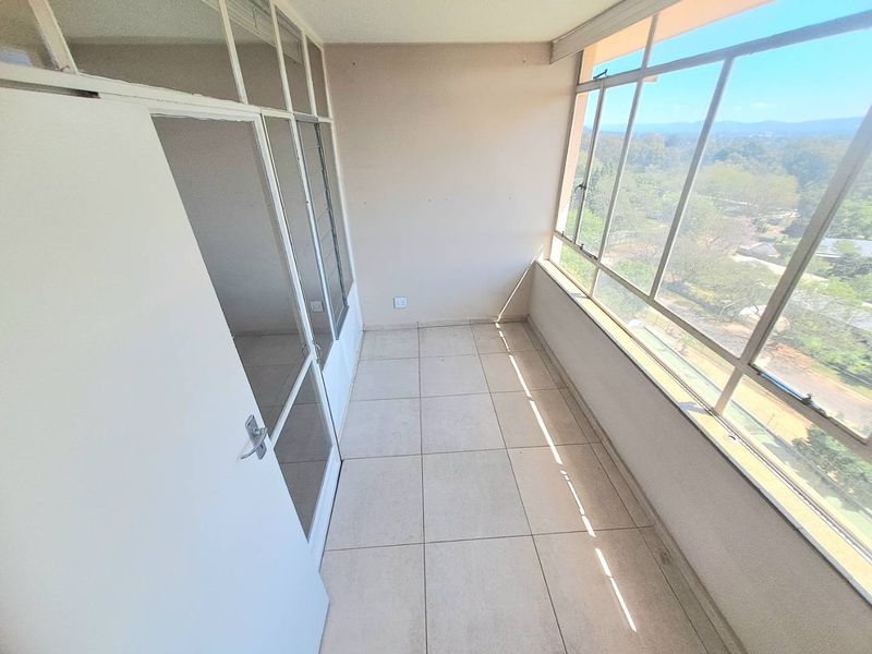 An enclosed balcony featuring tiled flooring and expansive glass windows offering natural light and scenic views.