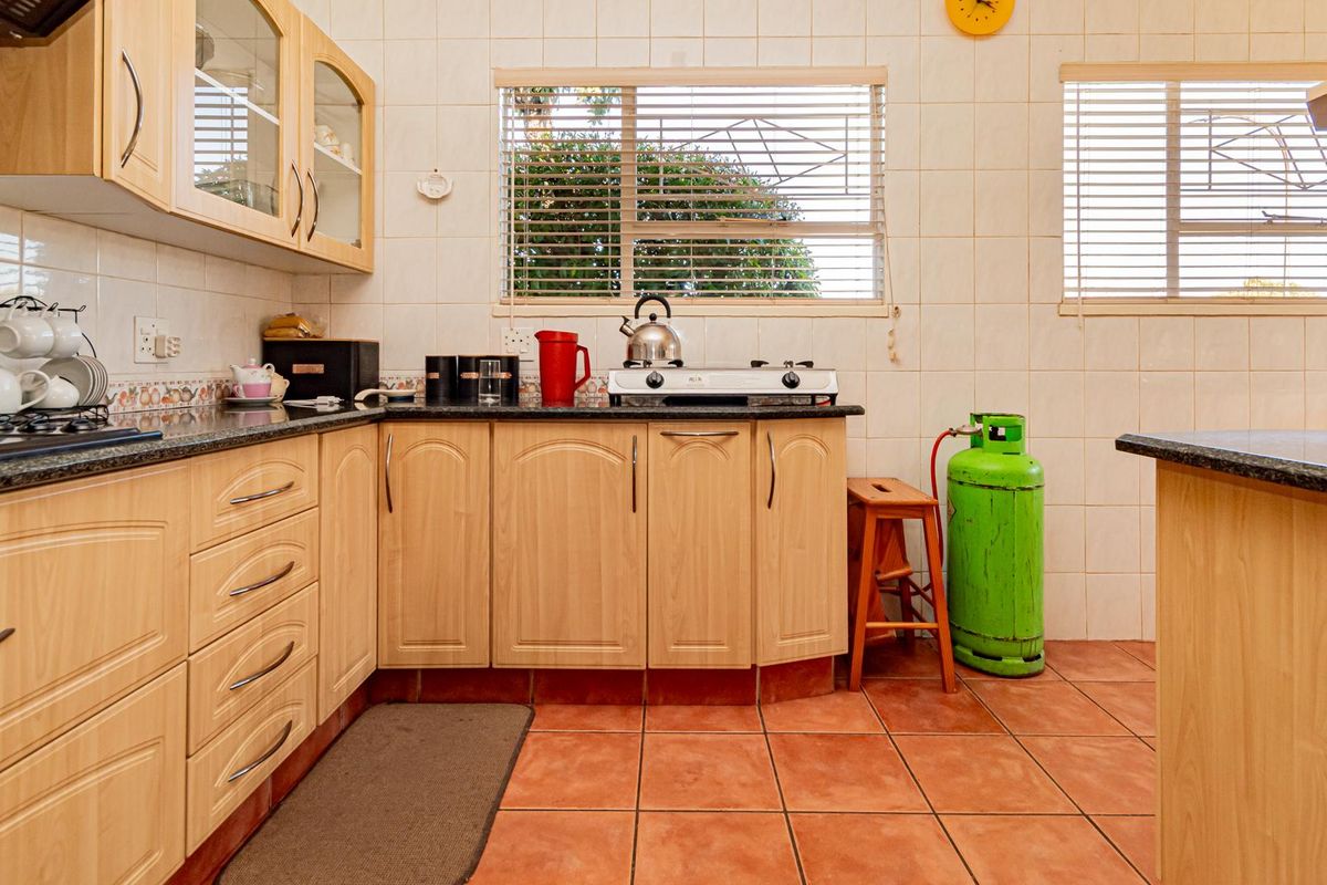 A functional kitchen featuring light wood-finish cabinetry, granite countertops, tiled backsplash, and ceramic floor tiles, equipped with a gas hob and venetian blinds.