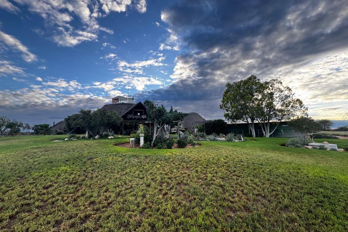 A wide-angle view of the rear exterior of a farm property featuring a traditional thatched roof and expansive, well-maintained garden grounds.