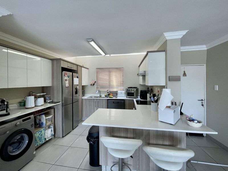 Modern kitchen featuring sleek cabinetry, stone countertops, a breakfast bar, and integrated laundry facilities, offering a functional and contemporary layout.