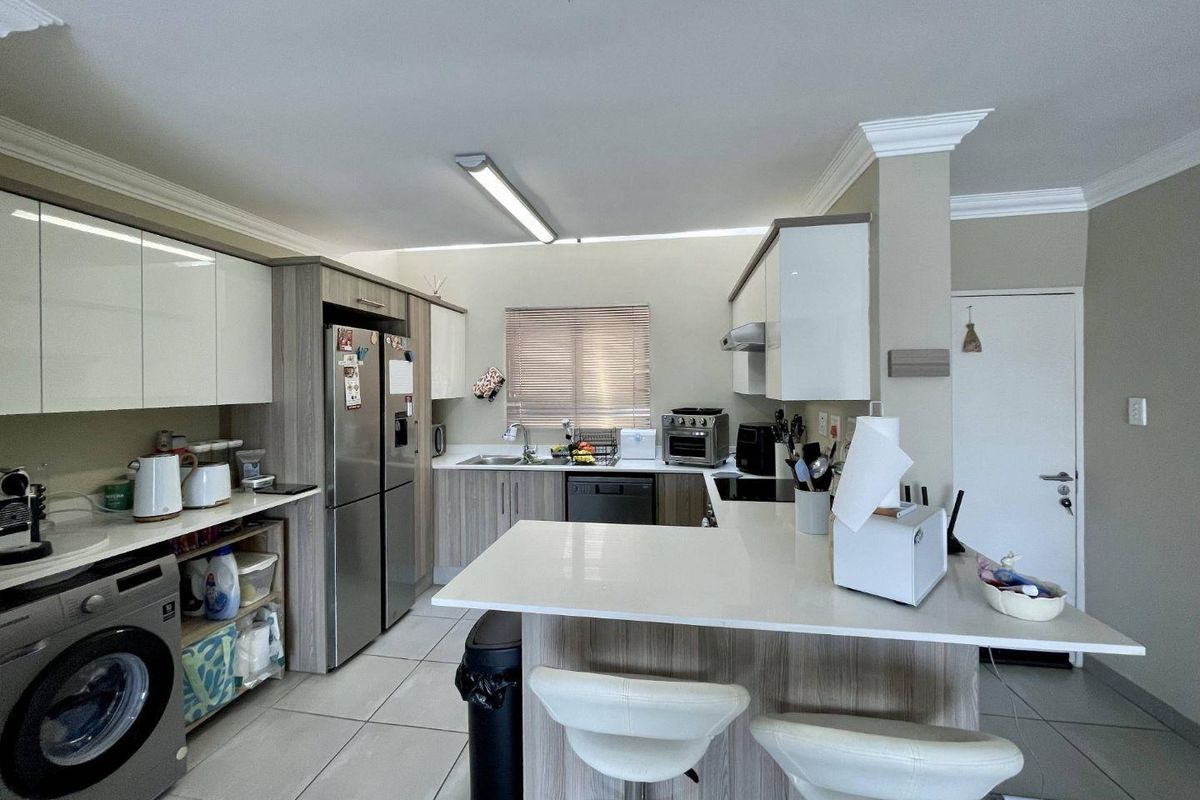 Modern kitchen featuring sleek cabinetry, stone countertops, a breakfast bar, and integrated laundry facilities, offering a functional and contemporary layout.