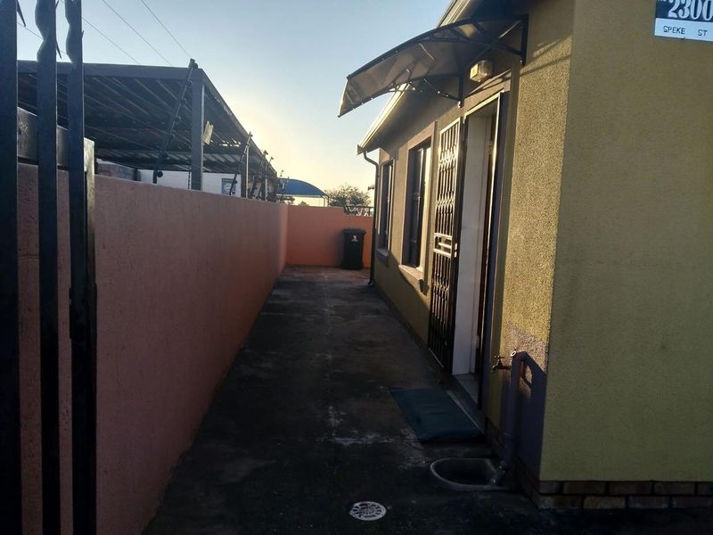 A side passage area featuring a concrete walkway, boundary wall, security gate, and an external tap with drainage.