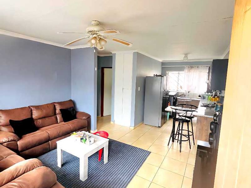 Open-plan living and kitchen area featuring tiled flooring, ceiling fan, and built-in cabinetry, offering a functional layout for modern apartment living.