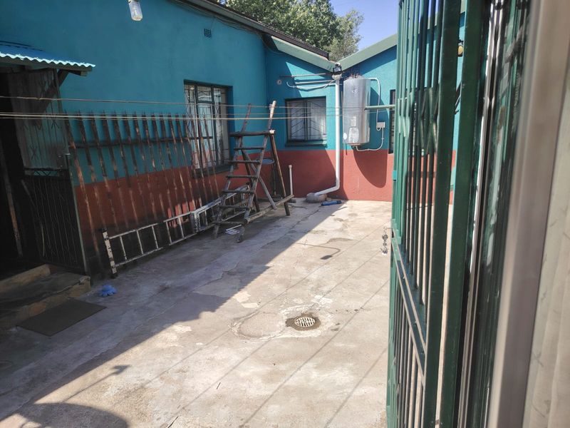 A paved rear courtyard area featuring an external geyser, security gates, and security bars on the windows.