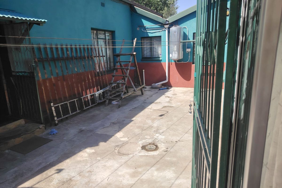 A paved rear courtyard area featuring an external geyser, security gates, and security bars on the windows.