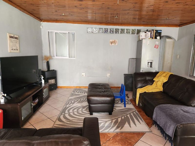 Living room featuring a timber-clad ceiling, tiled flooring, and a glass block feature window, providing a dated but functional living space.