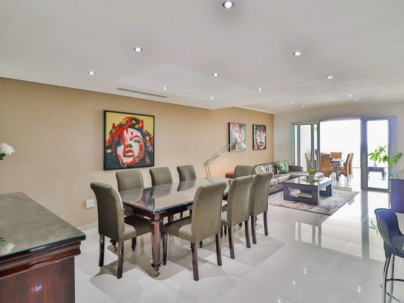 Spacious open-plan living and dining area featuring polished tiled flooring, recessed downlights, and large sliding glass doors leading to an outdoor balcony.