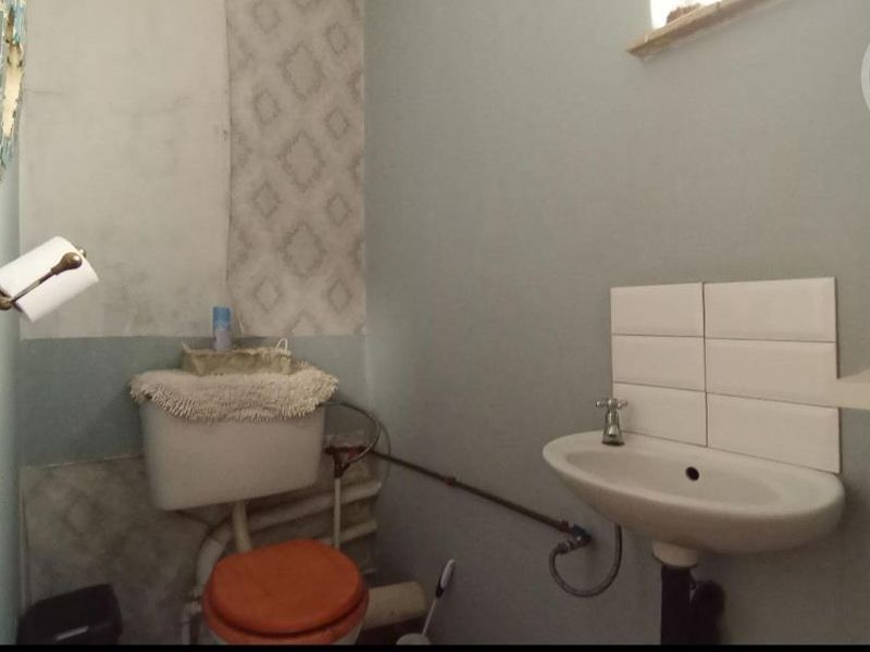 A small bathroom featuring a pedestal basin with tiled splashback and a toilet, currently requiring cosmetic updates and finishing of wall surfaces.
