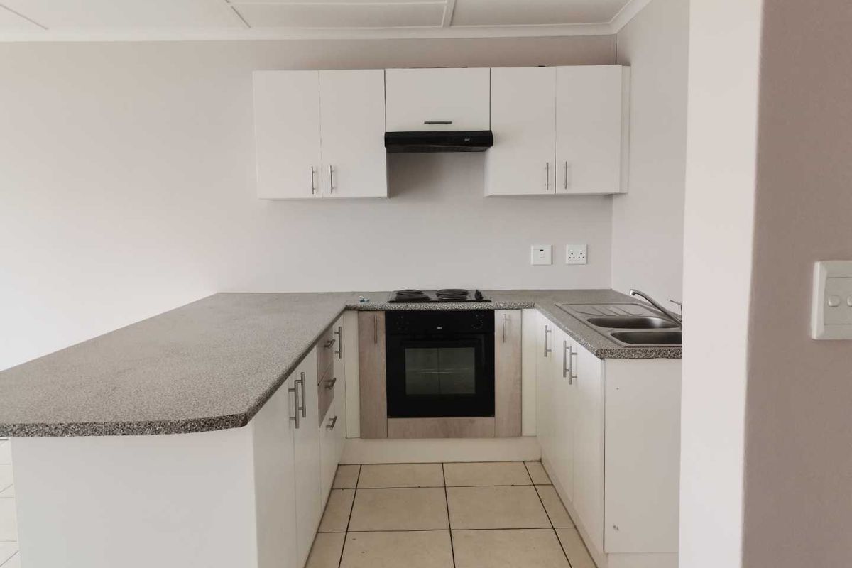 A functional kitchen featuring white cabinetry, granite-look countertops, a built-in oven, electric hob, extractor fan, and a double-basin stainless steel sink.