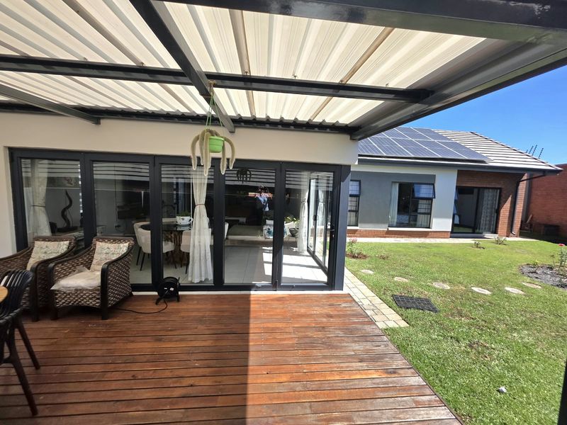 Covered patio area featuring timber decking and aluminium sliding doors, overlooking a well-maintained garden with solar panels visible on the main roof.