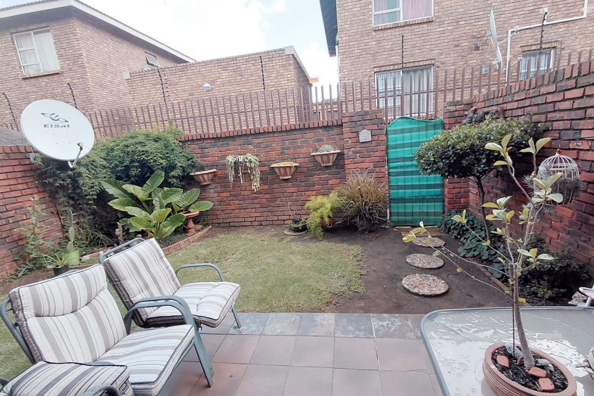 A private rear courtyard featuring a tiled patio area, a small lawn, and secure brick boundary walls with electric fencing.
