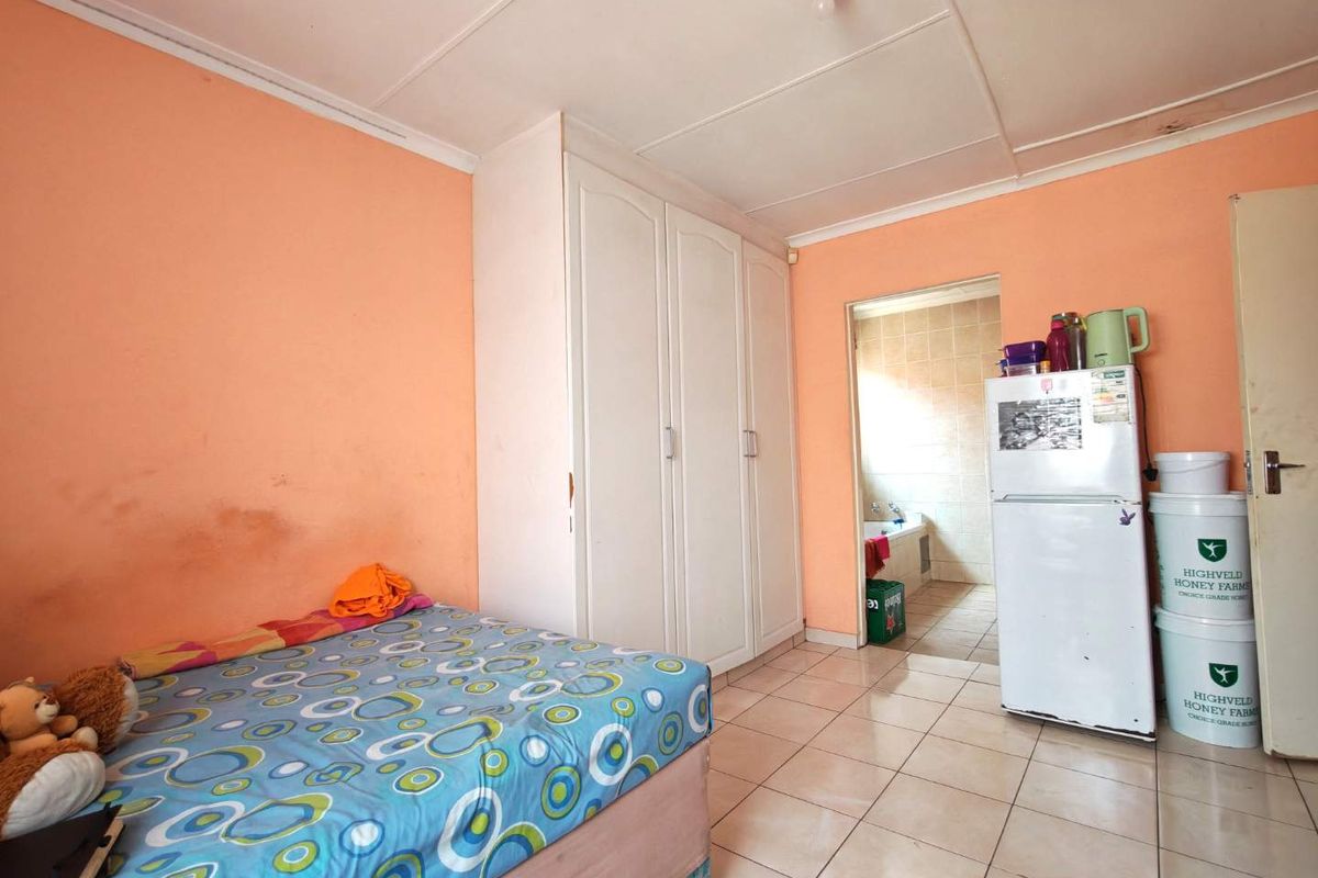 A bedroom featuring built-in cupboards and tiled flooring, with an adjoining bathroom visible through the doorway.
