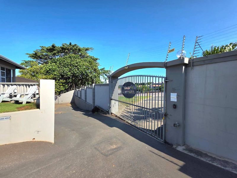 A secure business property entrance featuring a metal security gate, perimeter wall with electric fencing, and an asphalt driveway.