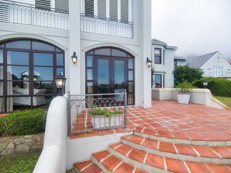 A spacious outdoor patio featuring terracotta tiling, wrought iron railings, and arched glass doors leading into the residence.